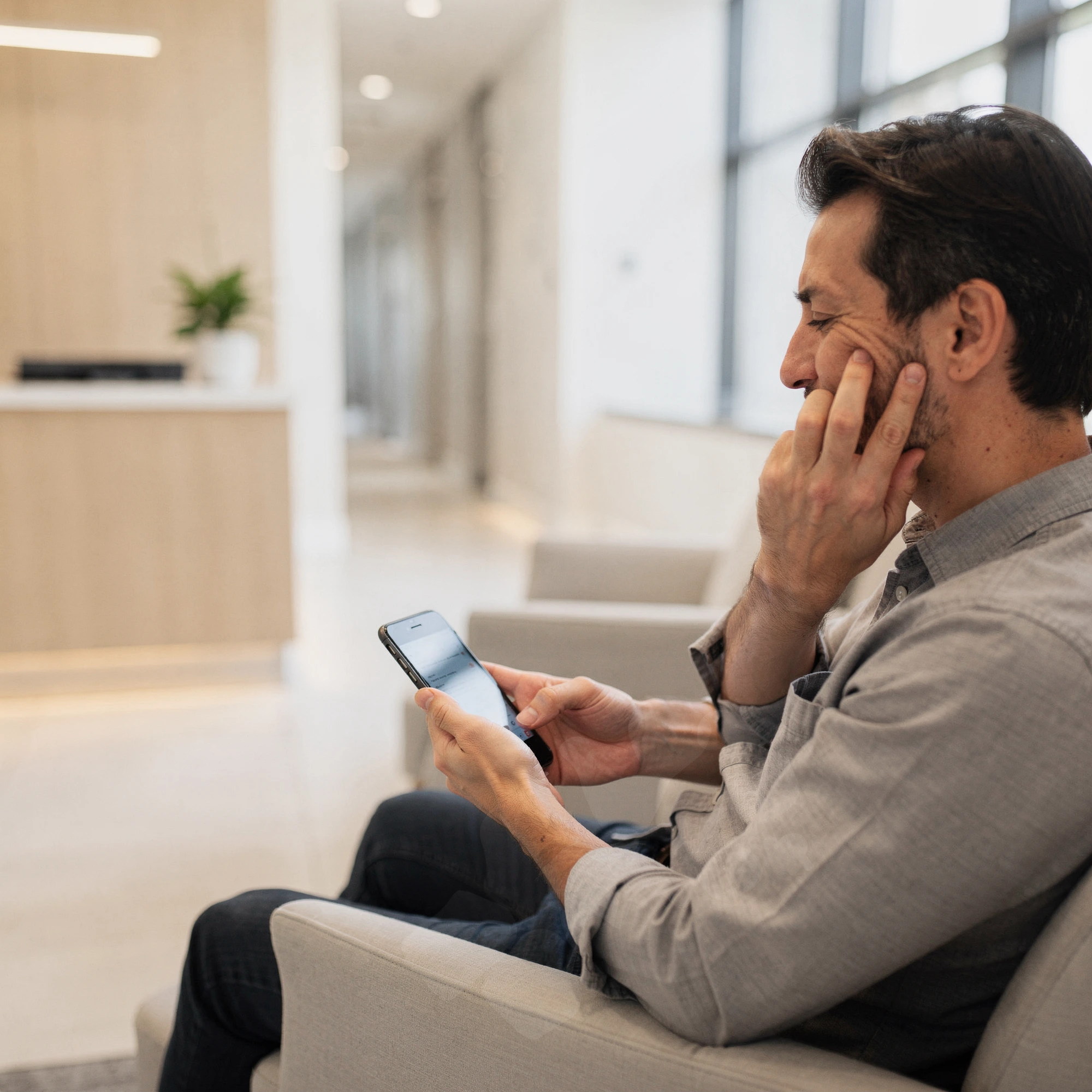 Man in dental waiting room holding his cheek in pain while looking at his phone